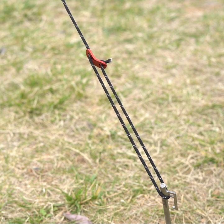 Winnerwell® guyline peg and cord securing camping equipment in a grassland area, showcasing the product’s functionality in different outdoor terrains.