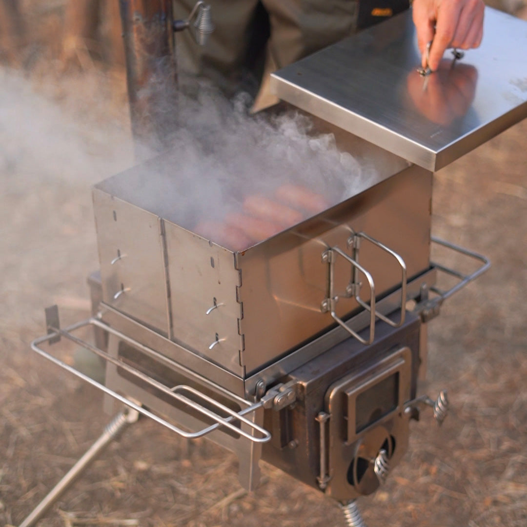 Winnerwell® Flat Smoker in action—wood - burning design provides heat for smoking meats, grilling food, or slow - cooking outdoors. Shown here in a campsite setting, highlighting its rugged, space - saving design for off - grid cooking experiences.
