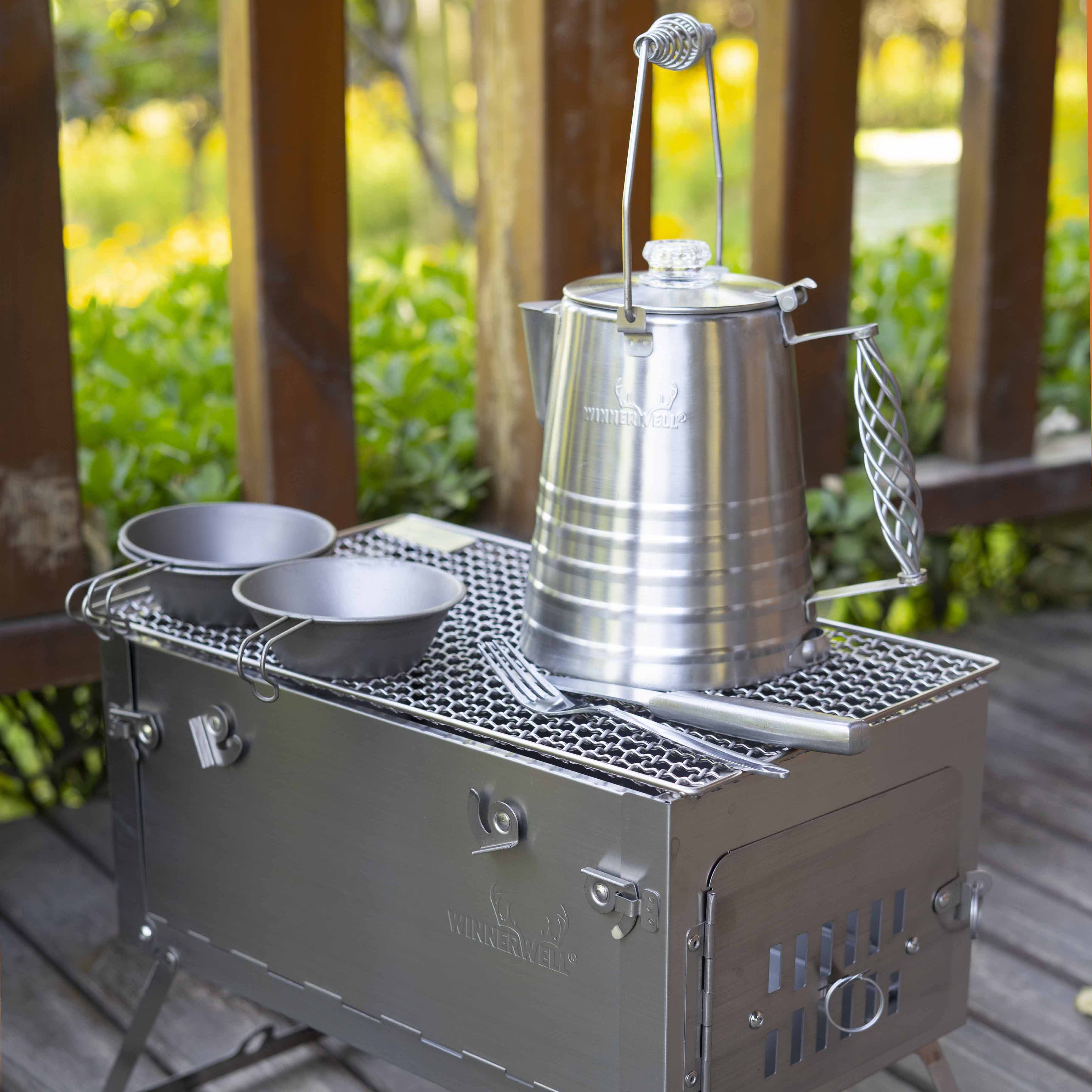 Winnerwell titanium stove used with cooking pots, kettle on grill grates, showcasing multi - use outdoor cooking setup for camping. Ideal for outdoor enthusiasts, perfect for preparing meals during camping trips, combining functionality and portability as a must - have camping gear.