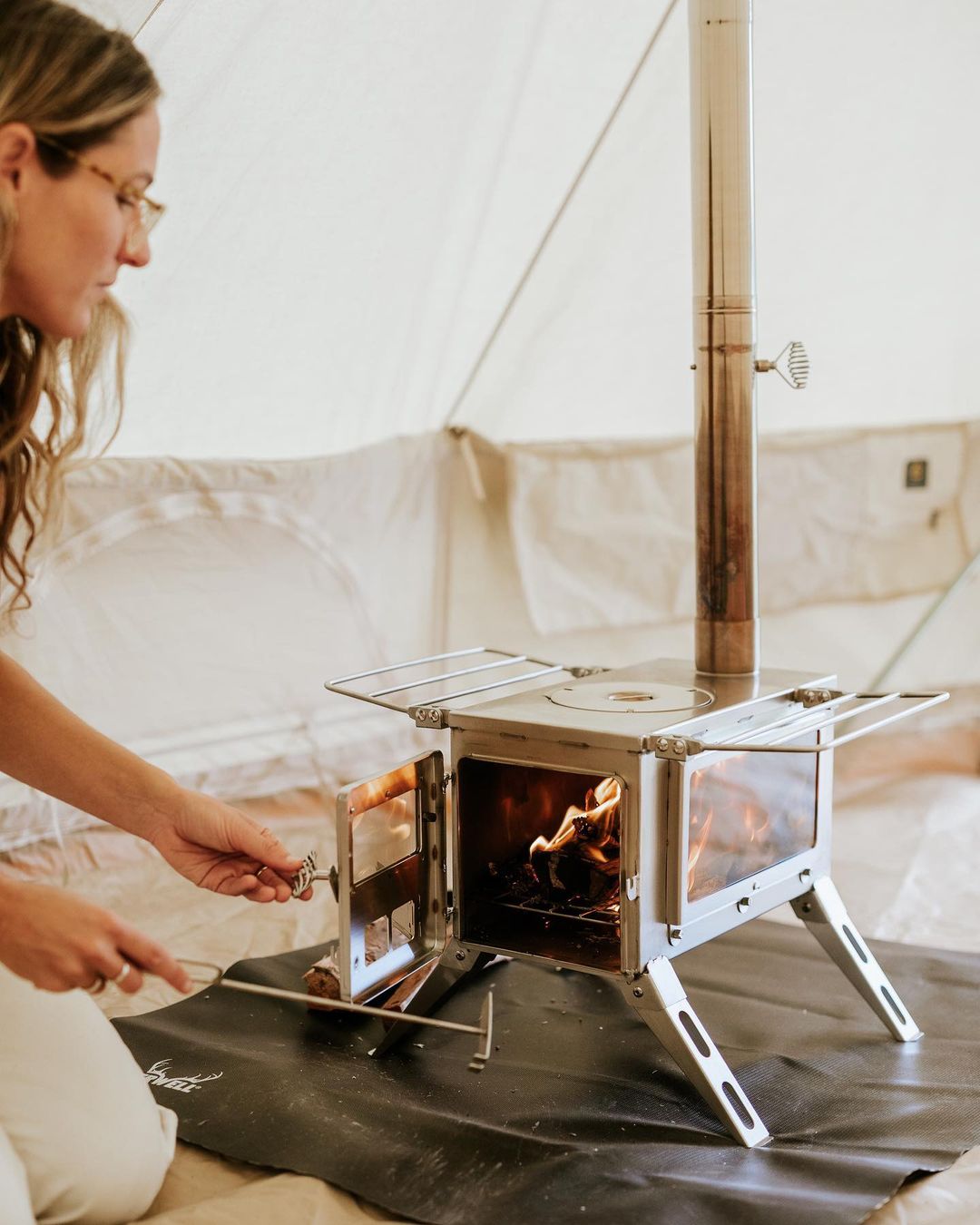 Winnerwell Nomad View stainless steel wood stove drying wet gear beside hot tent stove in cold weather camp