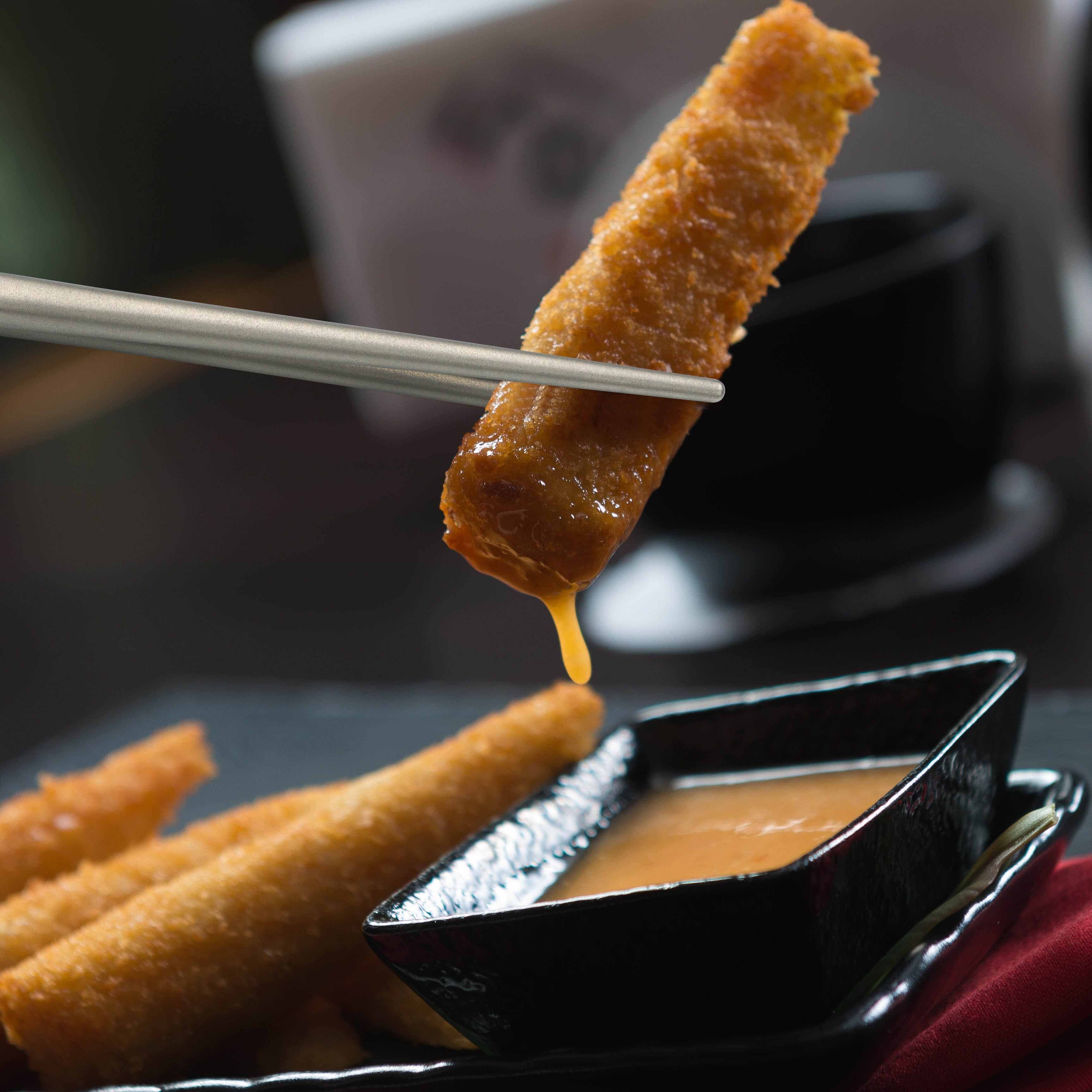 Winnerwell® square titanium chopsticks picking up a piece of food, illustrating their functionality in eating scenarios.