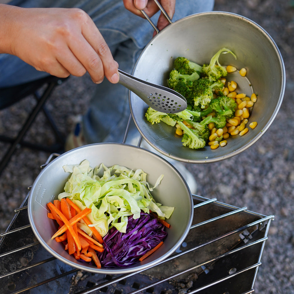 Hands cooking colorful vegetables in a Winnerwell® stainless steel Sierra cooking pot, demonstrating its practical application for outdoor meal preparation.