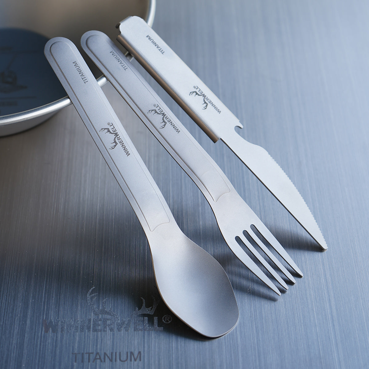 Winnerwell® titanium knife, fork, and spoon placed in a light - colored container, demonstrating convenient storage for outdoor adventures.