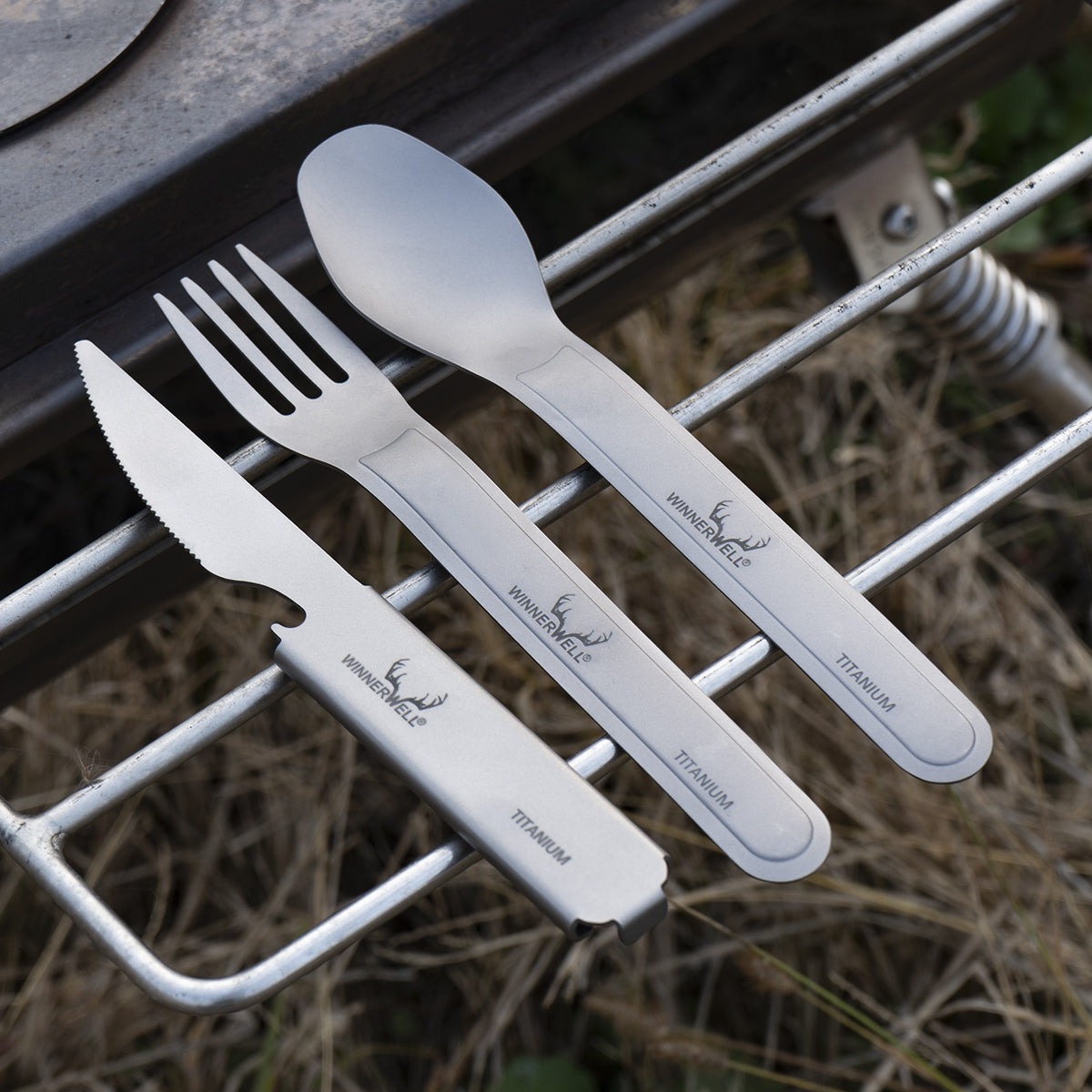 Winnerwell® titanium knife, fork, and spoon placed on a metal outdoor rack, highlighting their portability for camping or outdoor dining.
