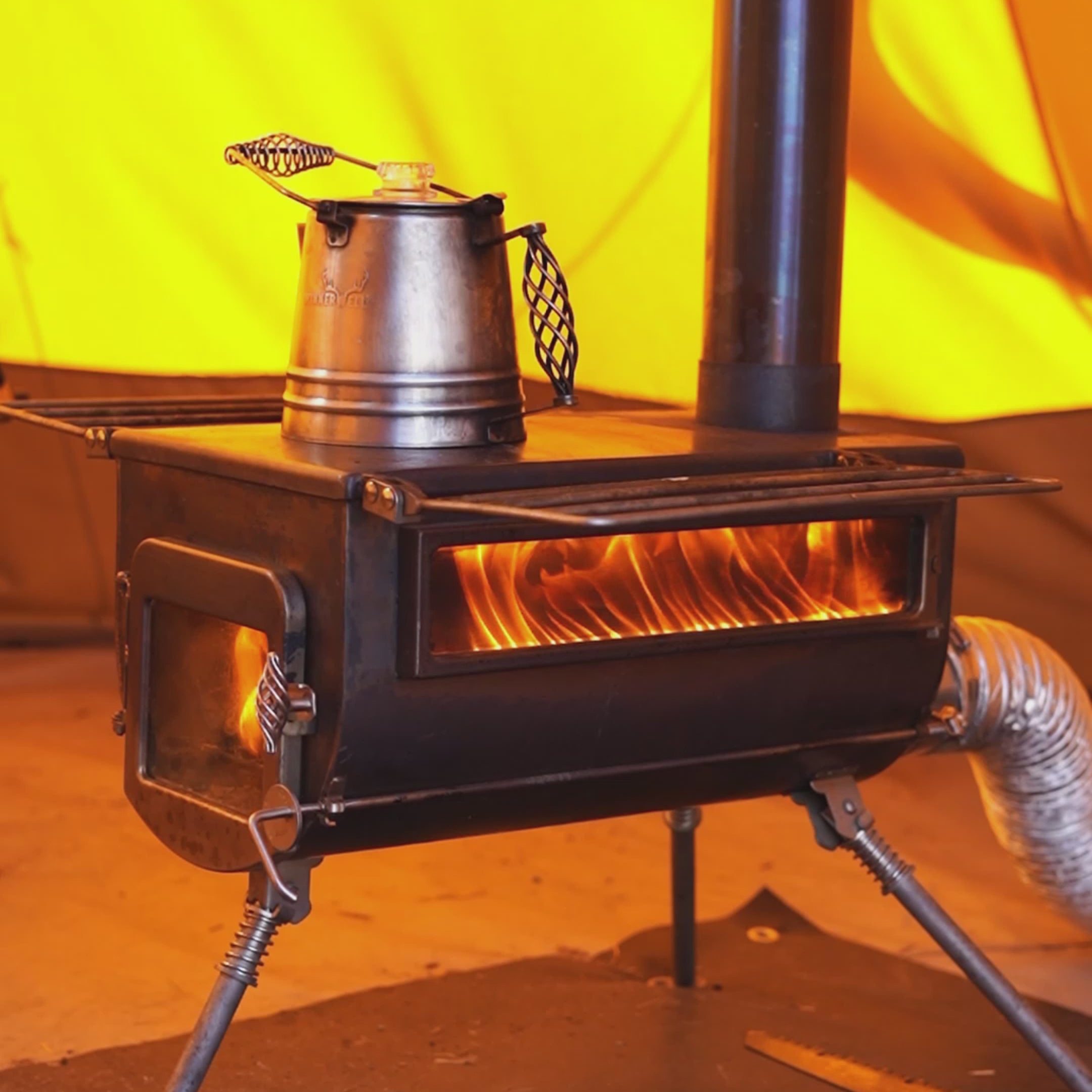 A fully assembled Winnerwell® Woodlander PLUS Double View External Air Wood Burning Tent Stove inside a winter camping tent, demonstrating its efficient heating capabilities with dual glass windows for fire monitoring.