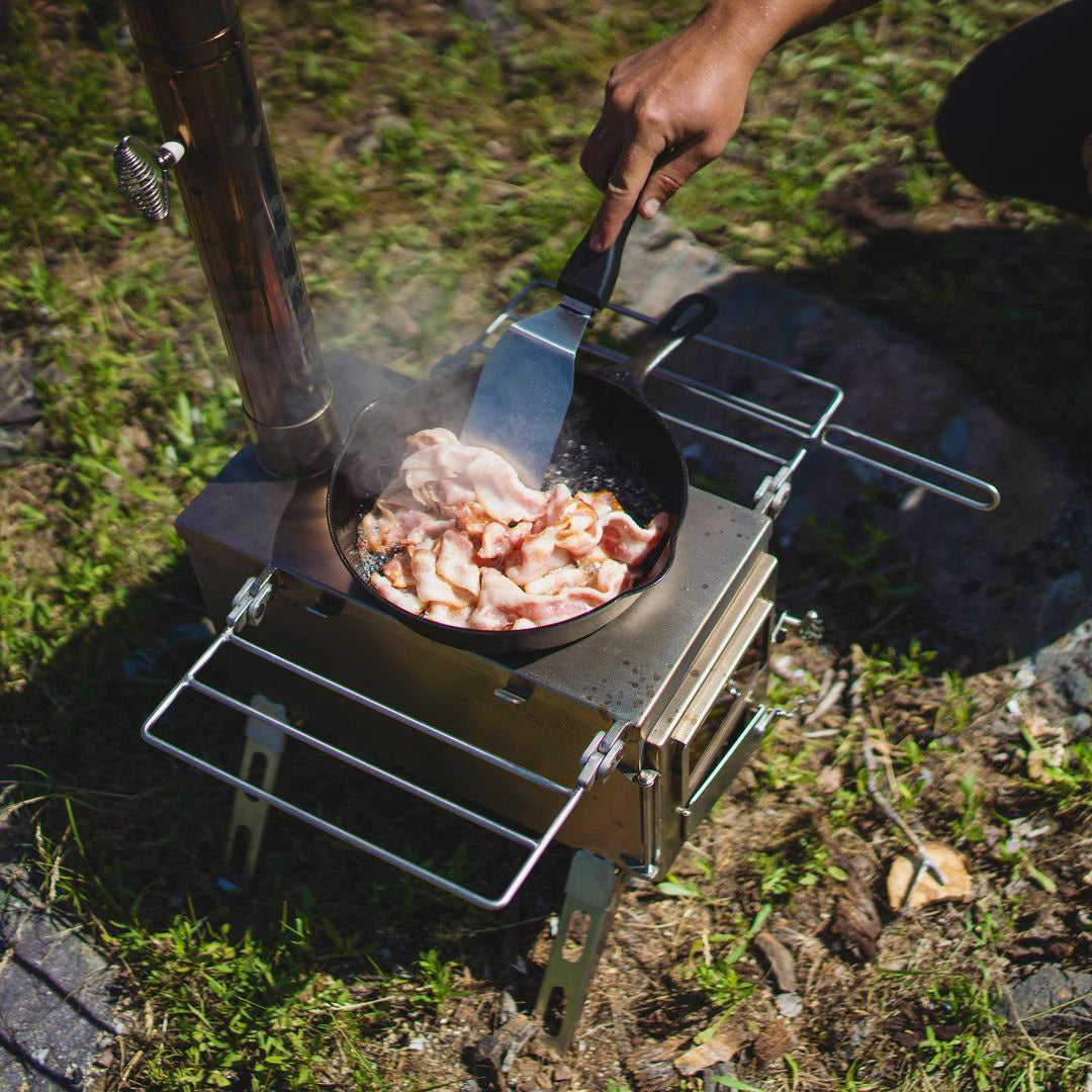 Close-up of Winnerwell® Nomad 1G Stove grilling meat, highlighting the stove’s heat distribution and grilling functionality for outdoor meals.