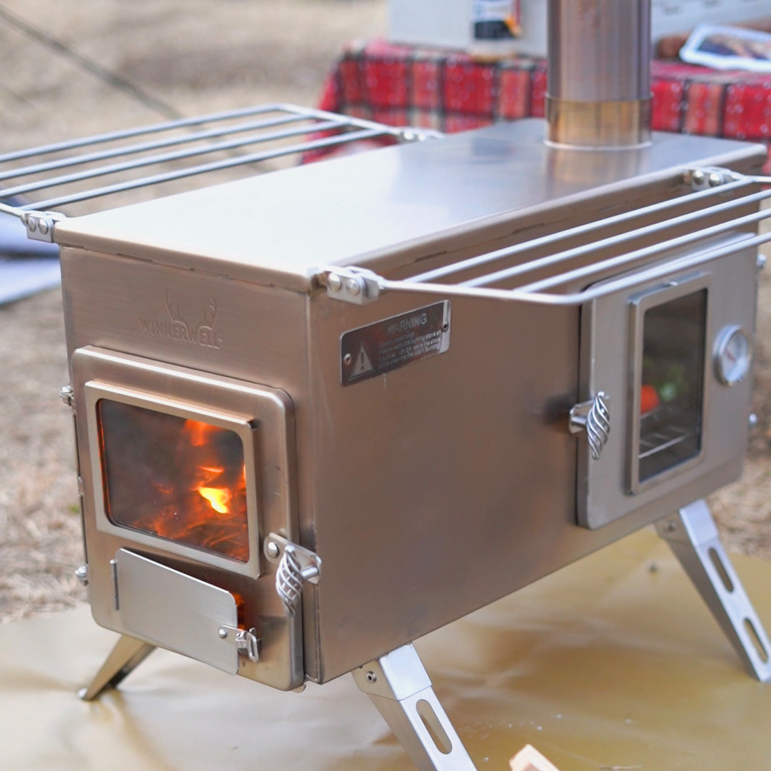 Winnerwell® Ovenstove Camping Stove in action—wood-burning design provides efficient heat for outdoor cooking, heating tents, or baking. Shown here in a campsite setting, highlighting its rugged, all-in-one outdoor cooking solution.